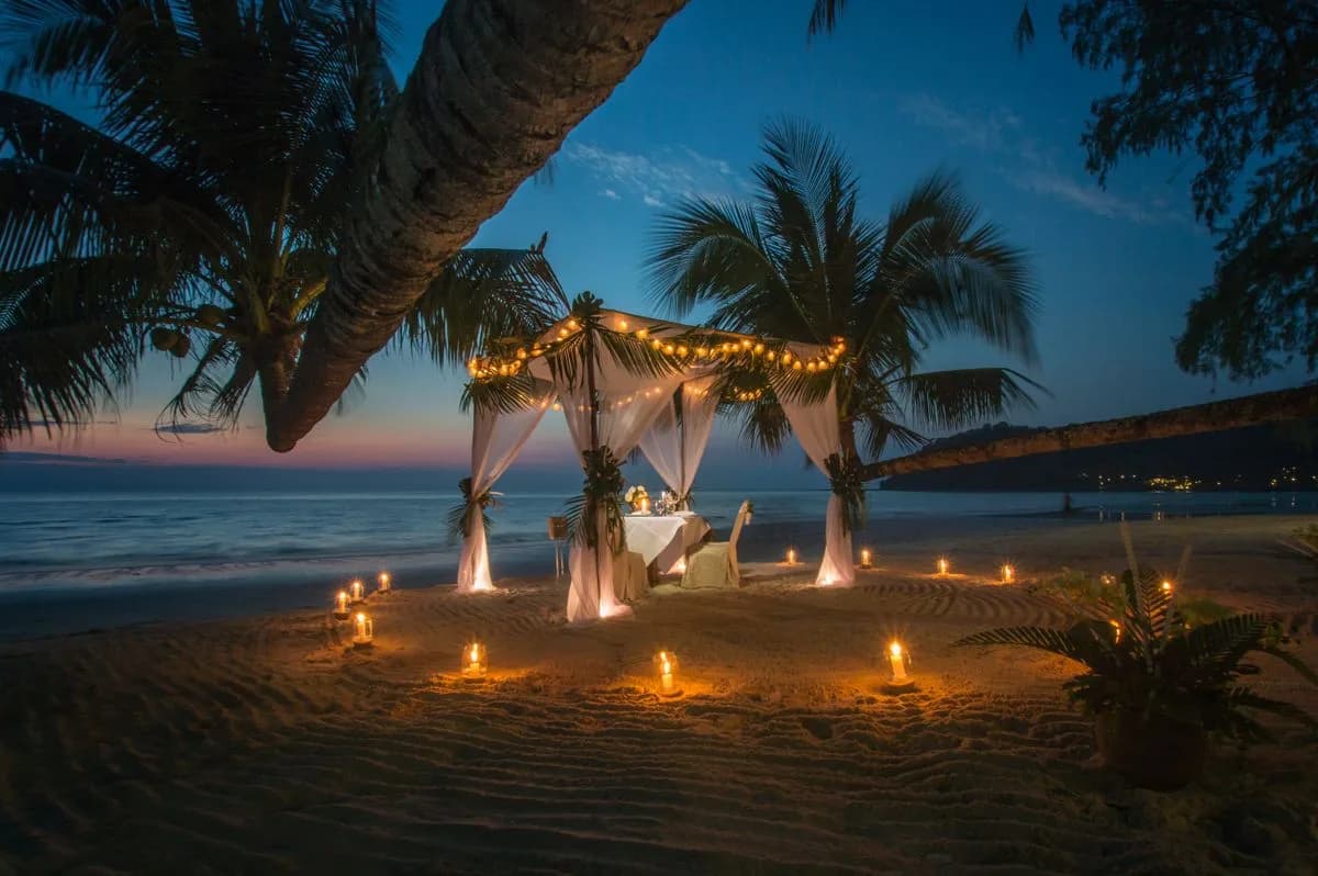 A candlelit dinner for two under a canopy on the beach at dusk