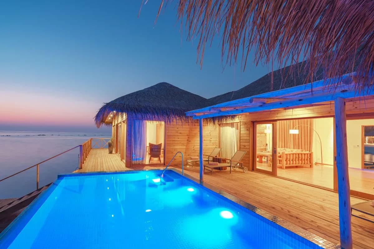An overwater villa with a lit pool at dusk