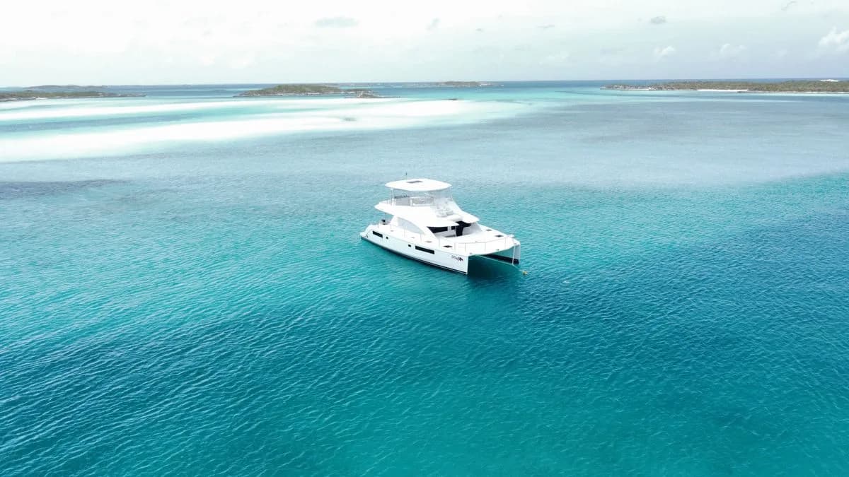 A white yacht at anchor on turquoise shallows, seen from above